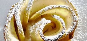 Freshly baked apple rose tarts sprinkled with powdered sugar resting on a white plate.