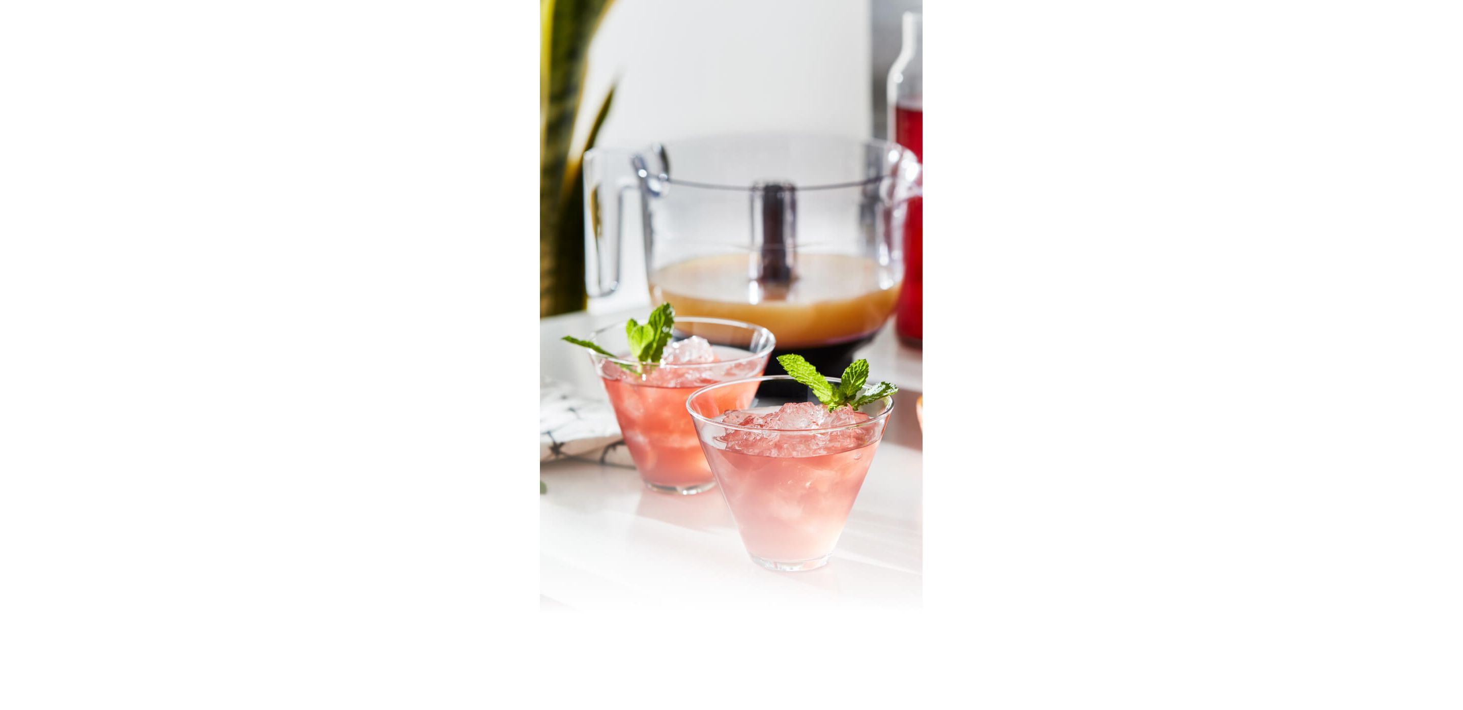 Two freshly made grapefruit cocktails resting on a bright kitchen counter with assorted citruses.