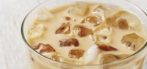 A cold glass of fresh lavender laced iced coffee with a white and purple straw.