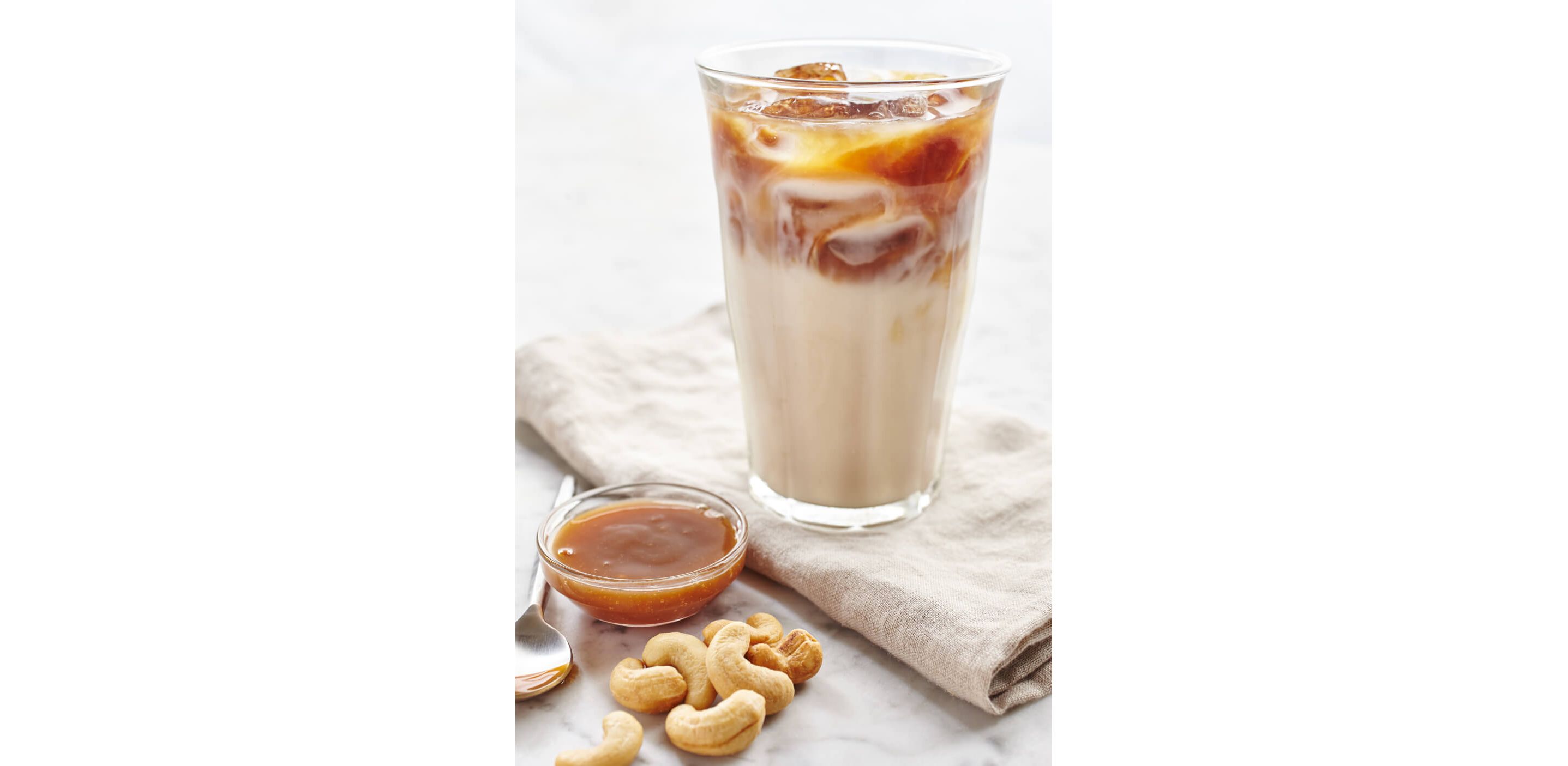 A cold glass of homemade iced coffee next two a small clear, bowl of caramel syrup.
