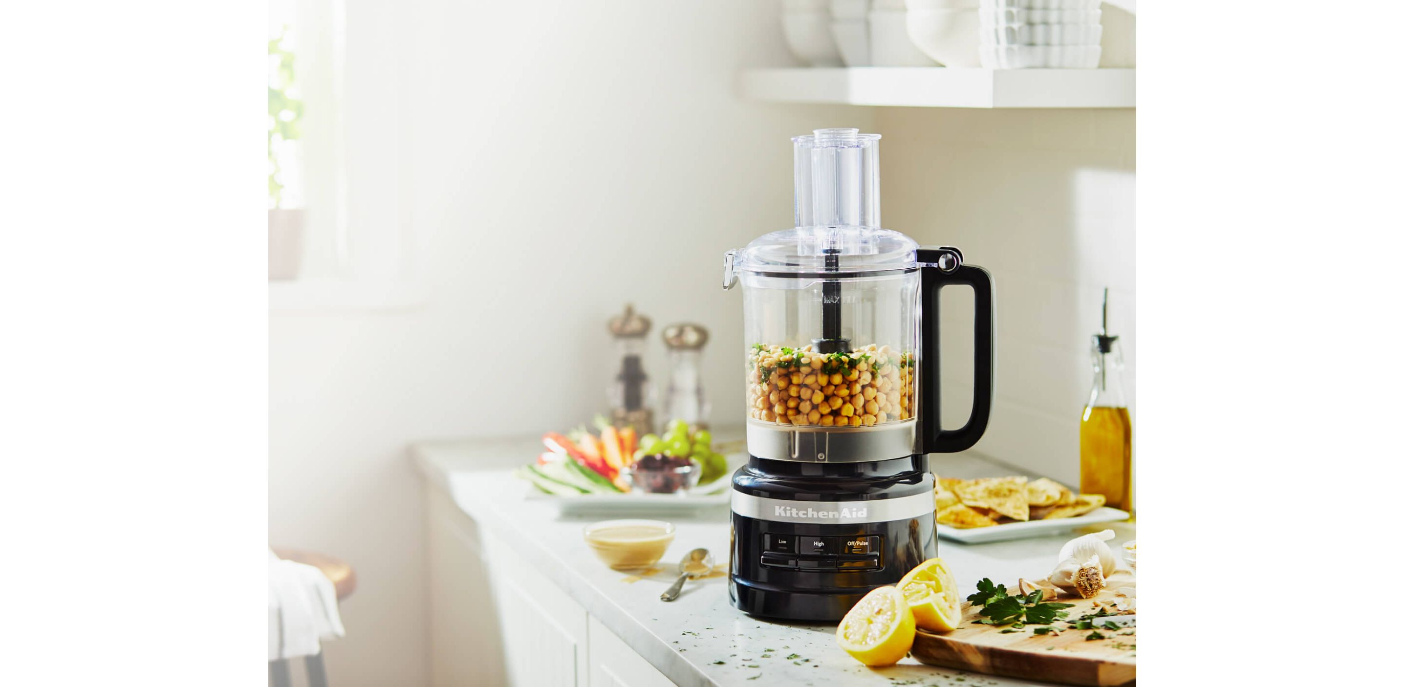 A Black Food Processor with chick peas and cilantro resting next to sliced lemons and other produce.
