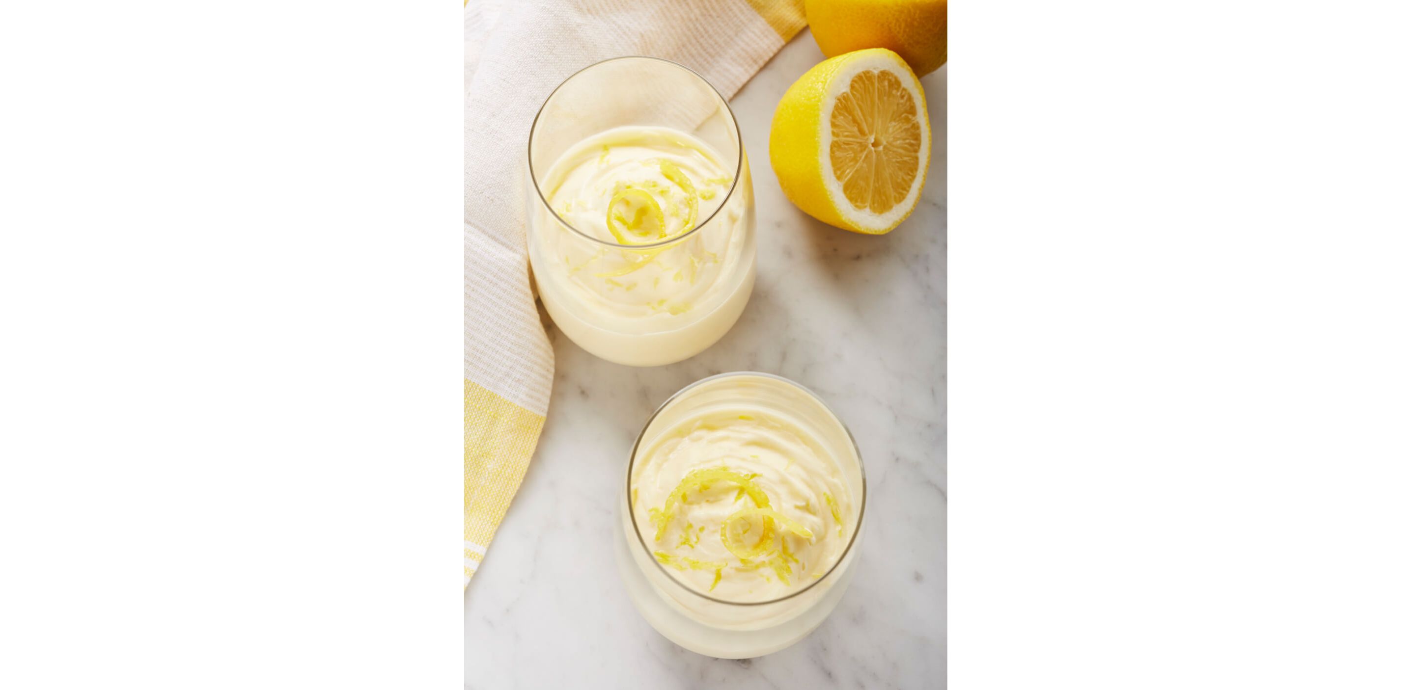 Two stemless wine glasses filled with lemon puree garnished with lemon zest.