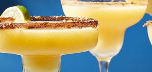 Margaritas glasses with seasoned rims filled with mango margarita garnished with sliced limes.