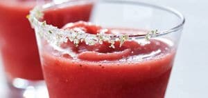 Two glasses of strawberry margaritas with salted rims garnished with limes.