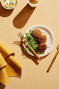 Three fried falafels next to fresh arugula on a clean, white plate.