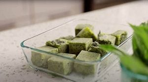 A glass dish filled with green frozen herb flavor bombs.