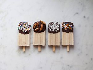 Four chocolate-dipped banana popsicles sprinkled with walnuts, shredded coconut and sprinkles.