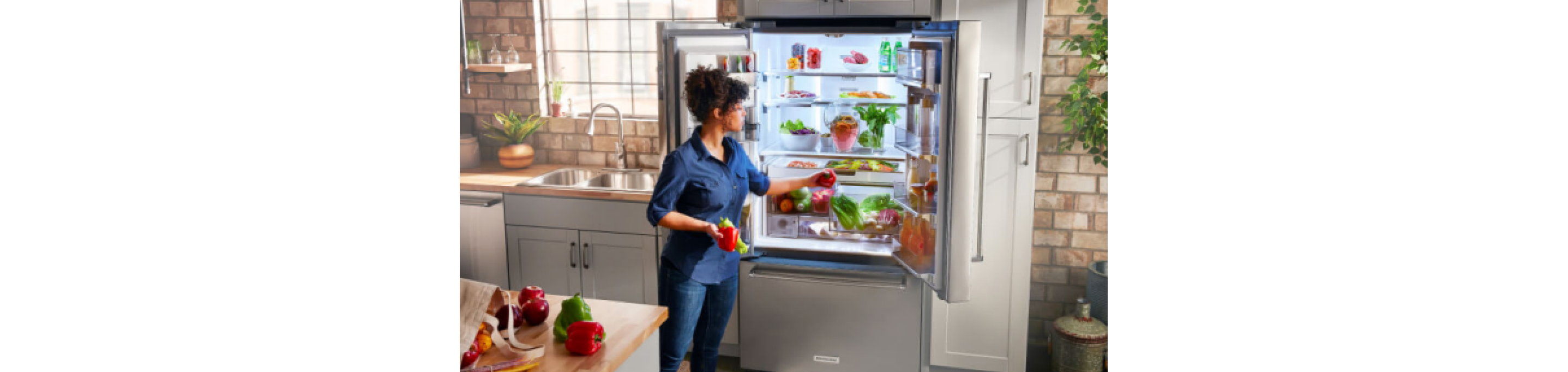 Woman loading vegetable into a french door refrigerator.