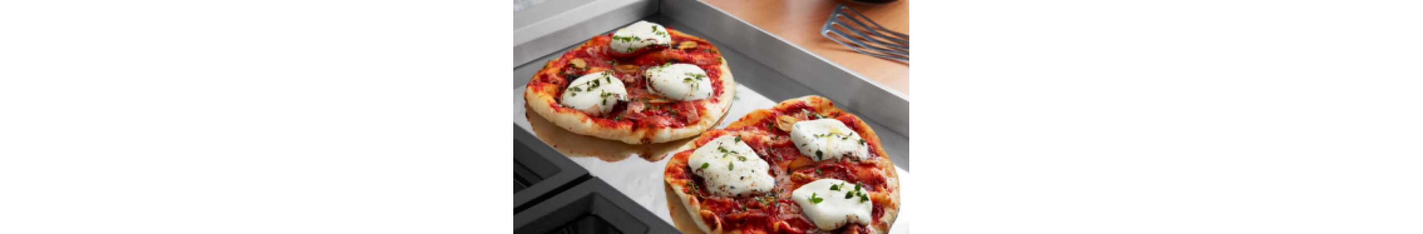 Two homemade Neapolitan pizzas cooking on a chrome electric griddle.