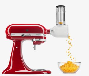 Red stand mixer with shredder attachment shredding cheddar cheese.