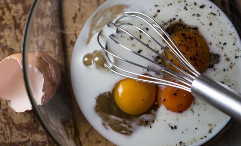 A whisk in a glass bowl with milk, eggs and spices