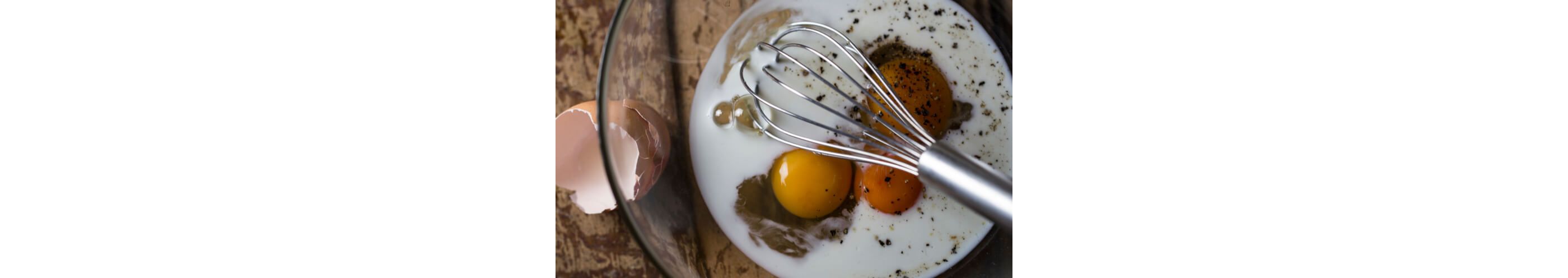 A whisk in a glass bowl with milk, eggs and spices