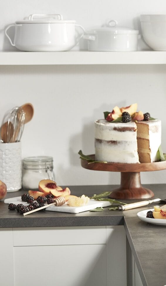 White frosted cake with fresh fruit on a wooden cake stand