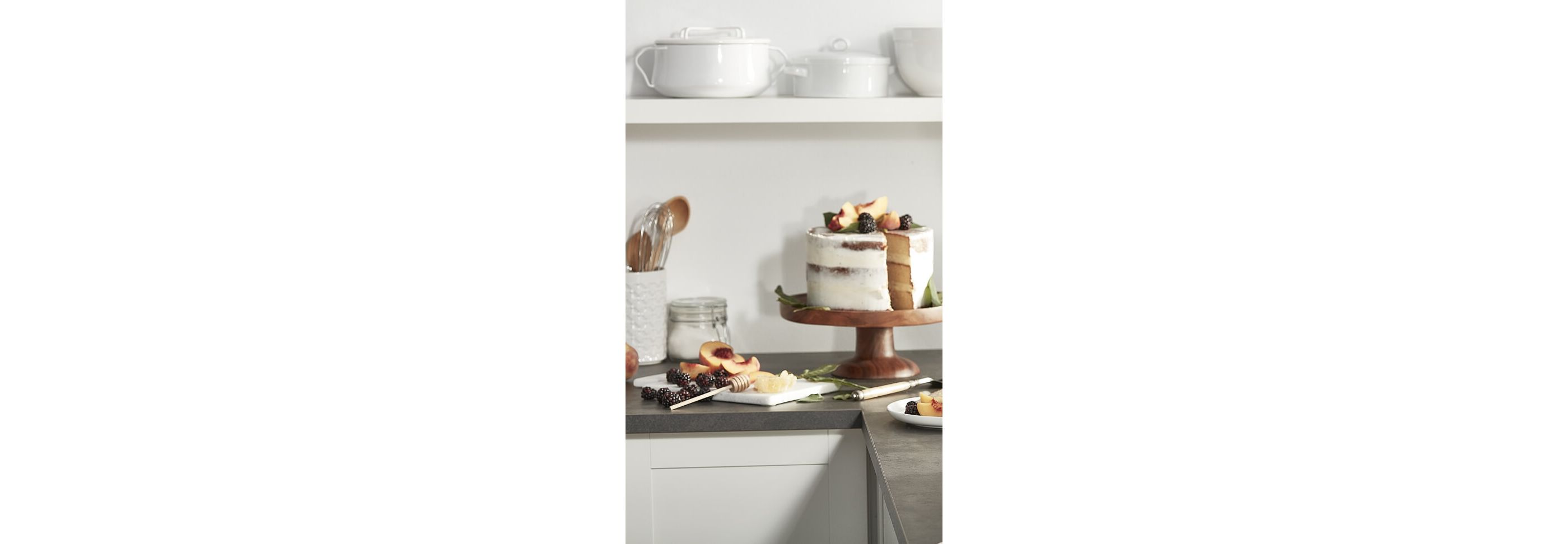 White frosted cake with fresh fruit on a wooden cake stand