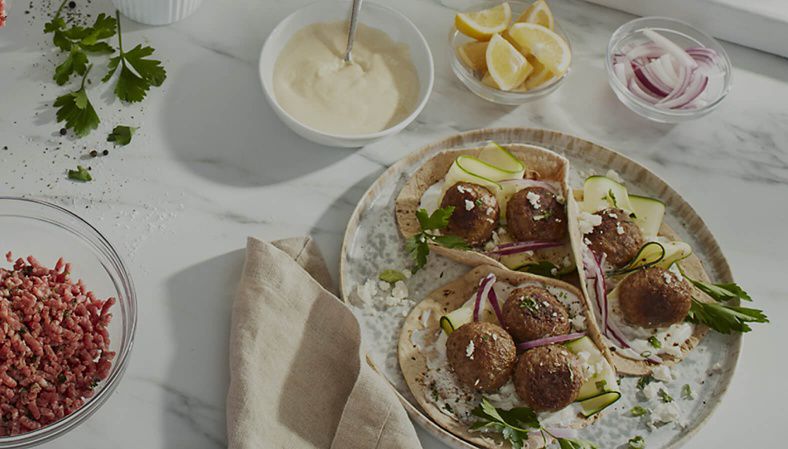 A plate of flatbreads with meatballs and toppings next to a bowl of ground meat and more toppings