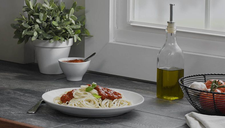A plate of fresh cooked pasta topped with marinara sauce next to sauce ingredients