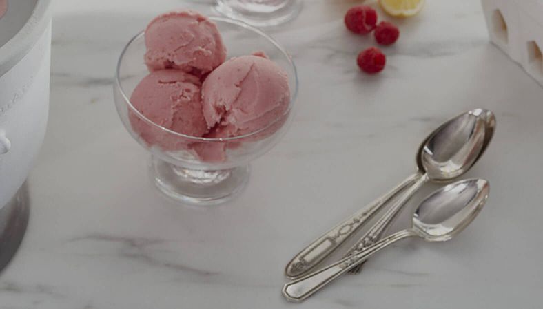 Bowl with scoops of ice cream on a countertop next to spoons