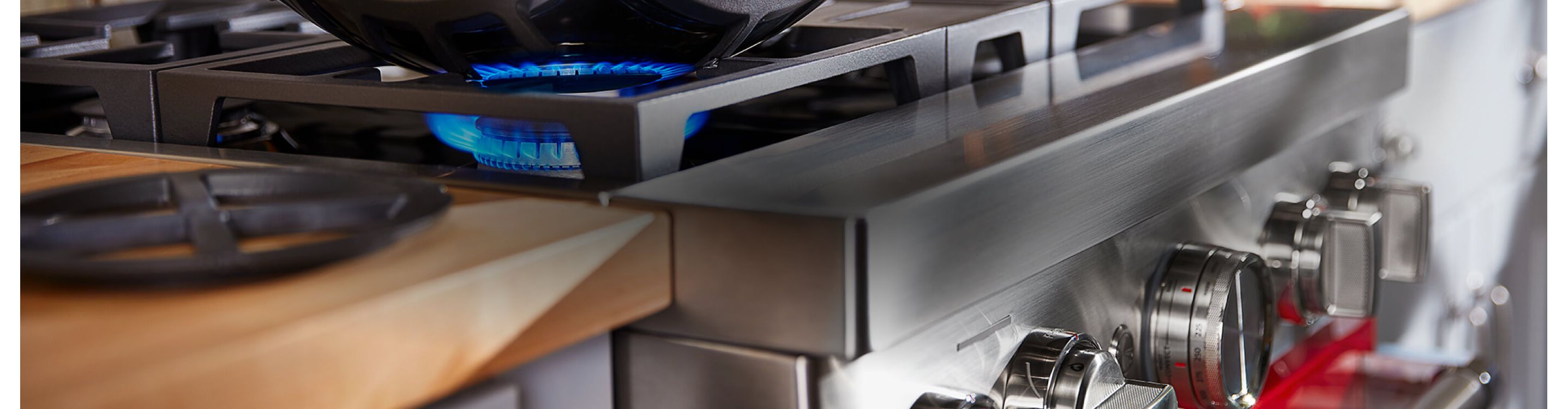 Close-up of commercial-style range, its handles, while a burner's flame heats a pot from below.