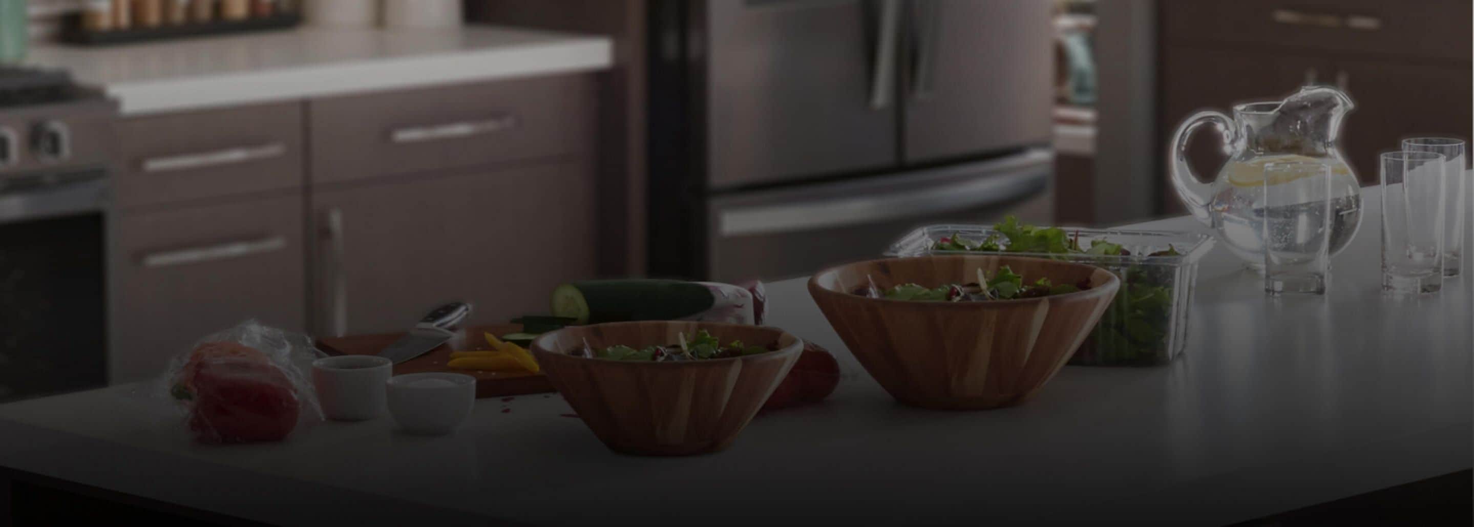 Une cuisine contemporaine avec deux bols à salade en bois entourés d’ingrédients variés et avec un pichet d’eau pure et propre