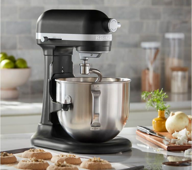 A Black KitchenAid® Bowl-Lift Stand Mixer next to different pastries and freshly baked chocolate chip cookies on baking sheets.