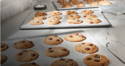 A Black KitchenAid® Bowl-Lift Stand Mixer next to different pastries and freshly baked chocolate chip cookies on baking sheets.