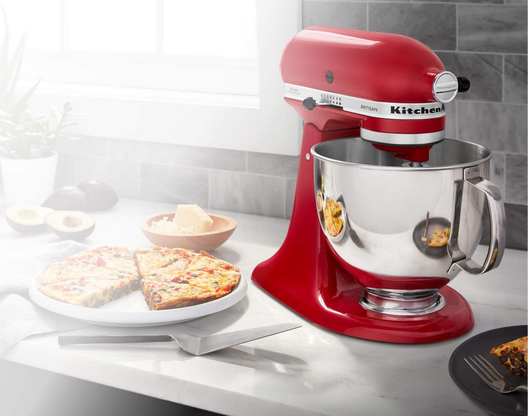 A Red KitchenAid® Tilt-Head Stand Mixer on a countertop, with different ingredients making homemade pizza.
