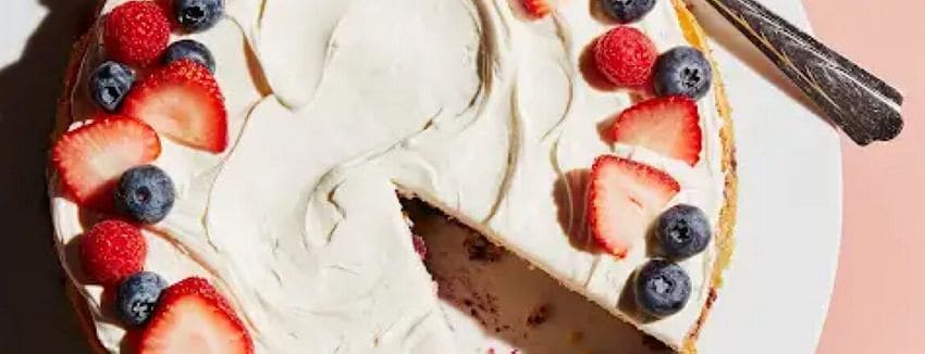 An almond cake garnished with fresh strawberries and blueberries.
