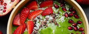 A green smoothie bowl garnished with fresh fruit, seeds and shaved coconut.