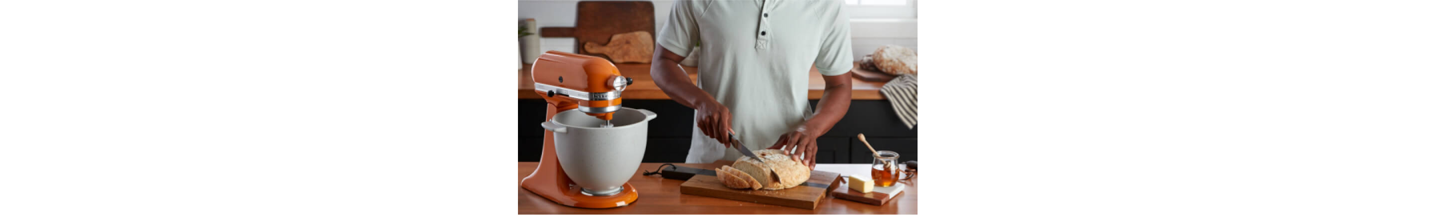 A person slicing a loaf of freshly baked bread, using a KitchenAid® Stand Mixer and the bread baking attachment. 