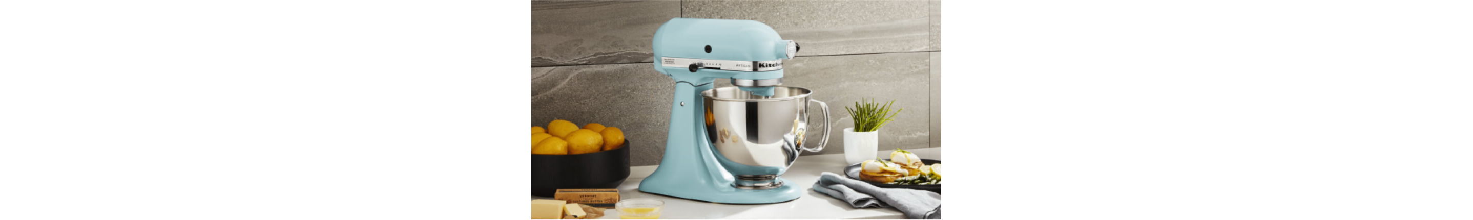 A blue KitchenAid® Stand Mixer on a countertop surrounded by different ingredients. 