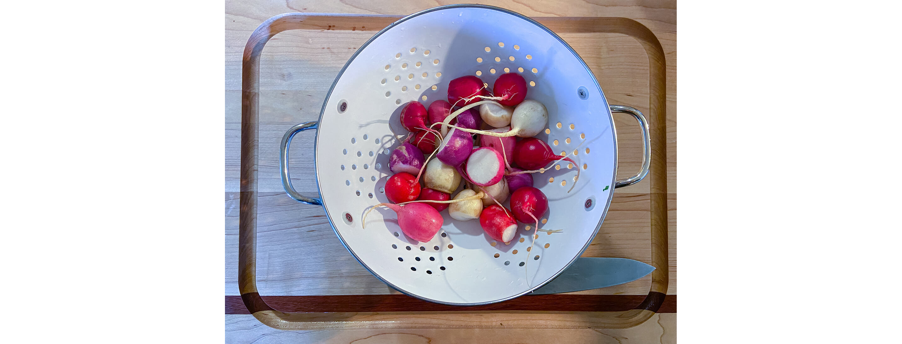 A metal strainer filled with freshly cleaned, whole radishes.