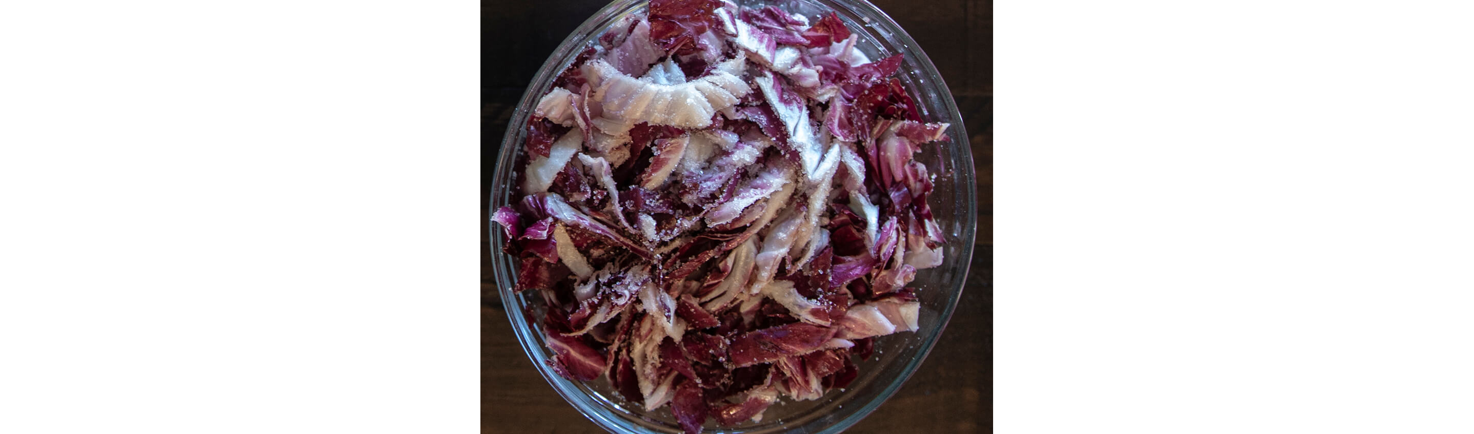 A glass bowl filled with sliced, salted red cabbage.
