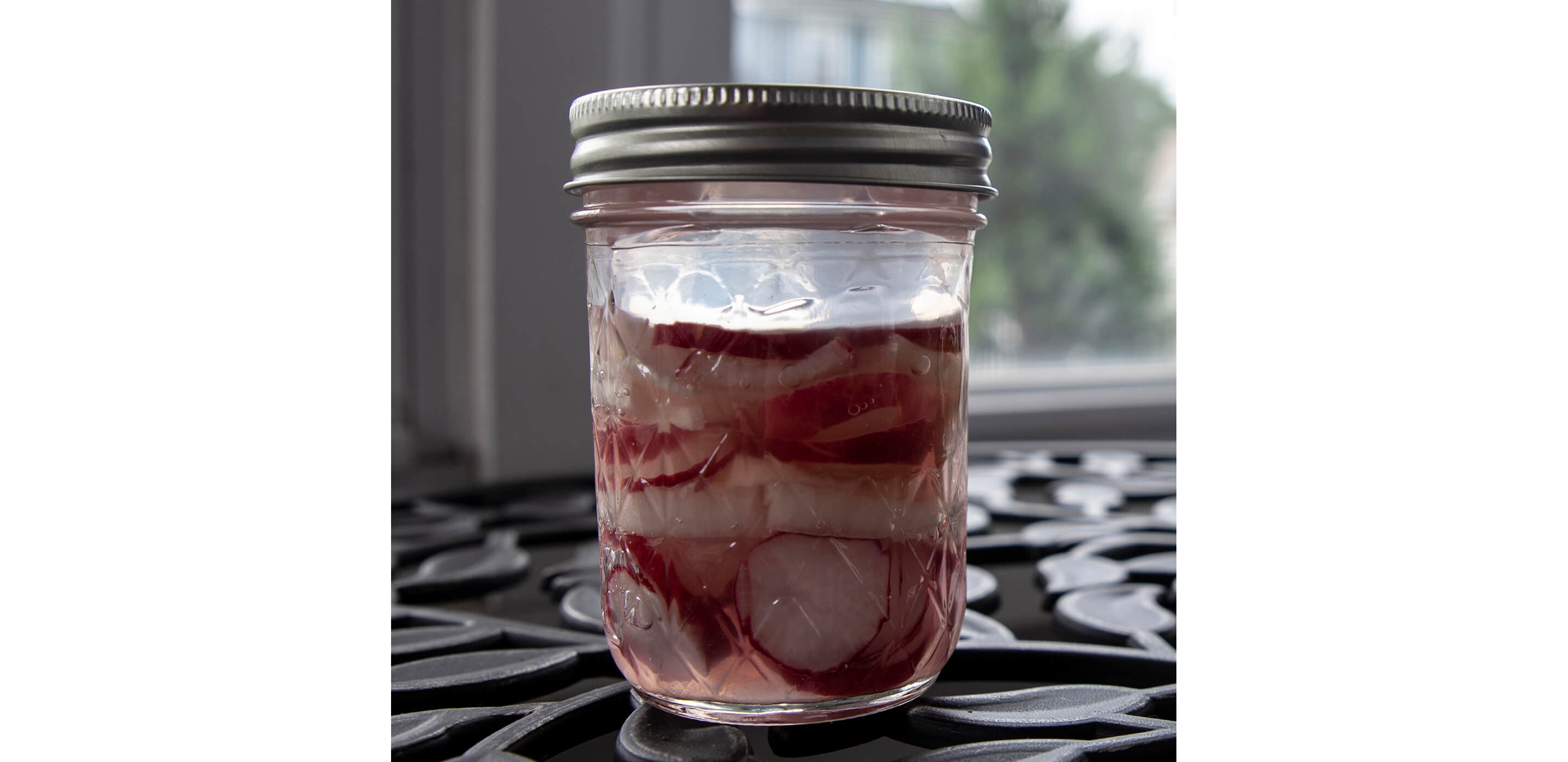 A sealed, glass jar holding fermented radishes.