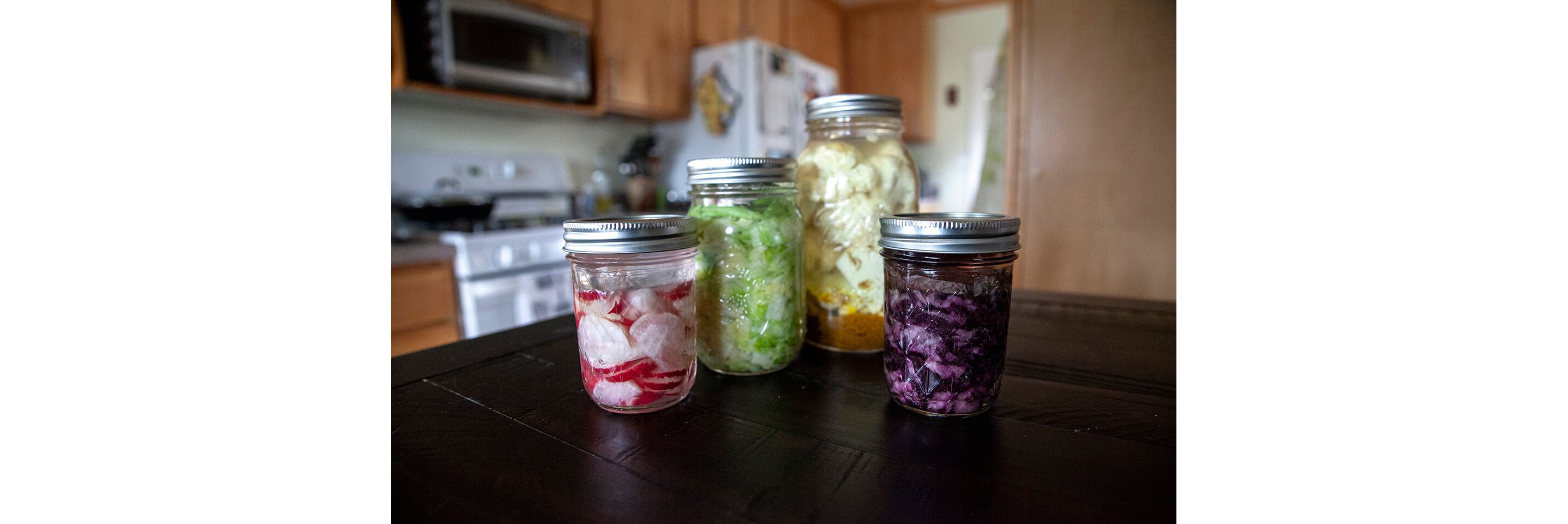Four sealed, glass jars holding a variety of fermented vegetables.