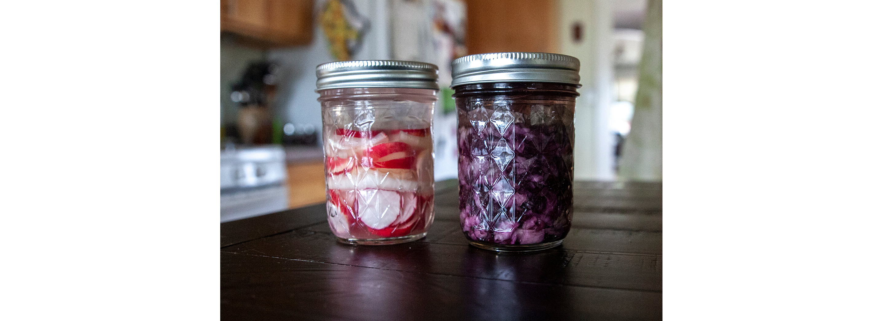 Two glass jars holding fermented radishes and red cabbage.