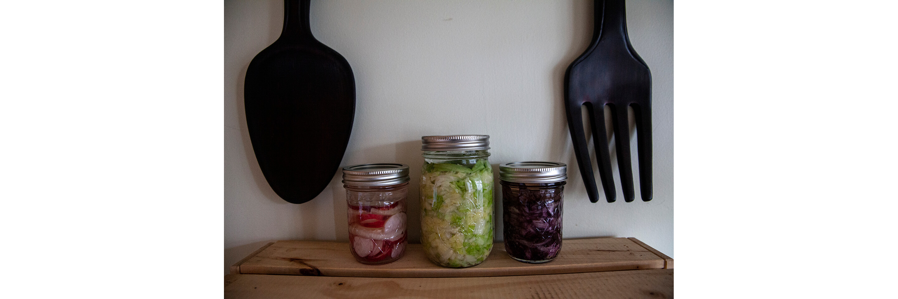 Three glass jars holding fermented radishes, red cabbage and green cabbage.