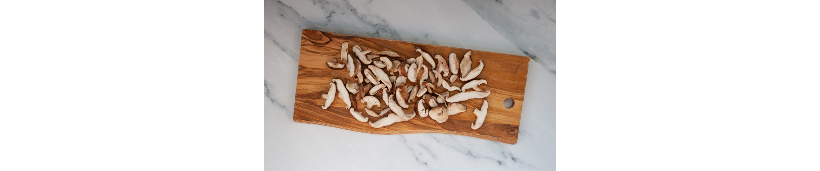 Sliced mushrooms resting on a wooden cutting board.
