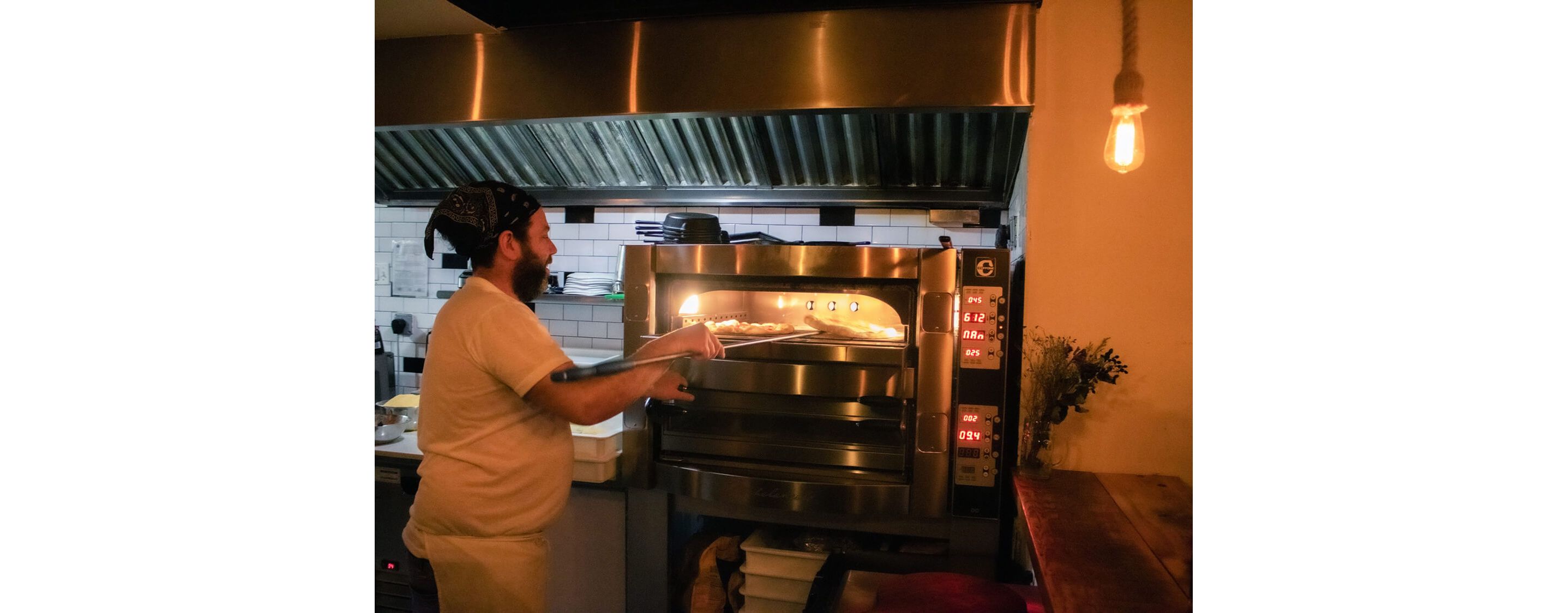 A man expertly working pizzas into a stainless steel pizza oven in a restaurant kitchen.