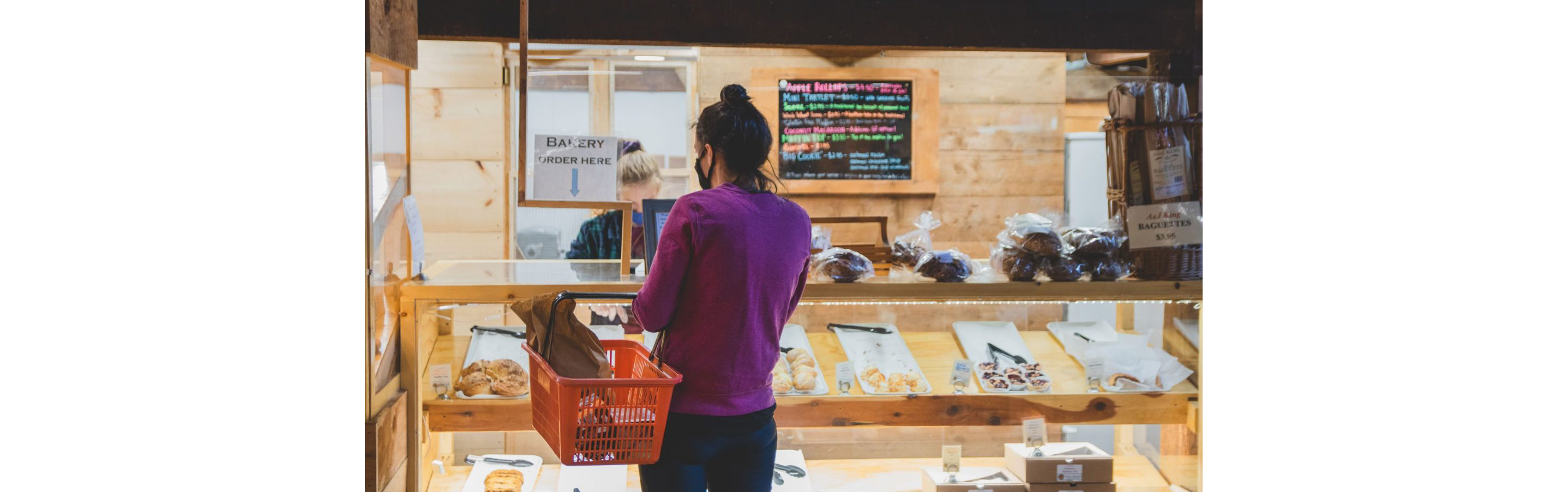 A young woman waiting for pastries as she carries her shopping basket.