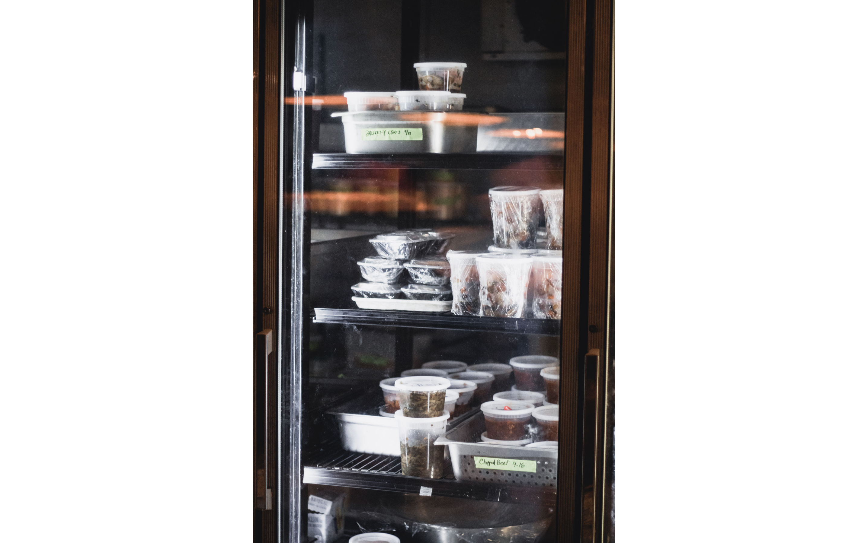 A refrigerator filled with containers of assorted meats, briskets and other eats.