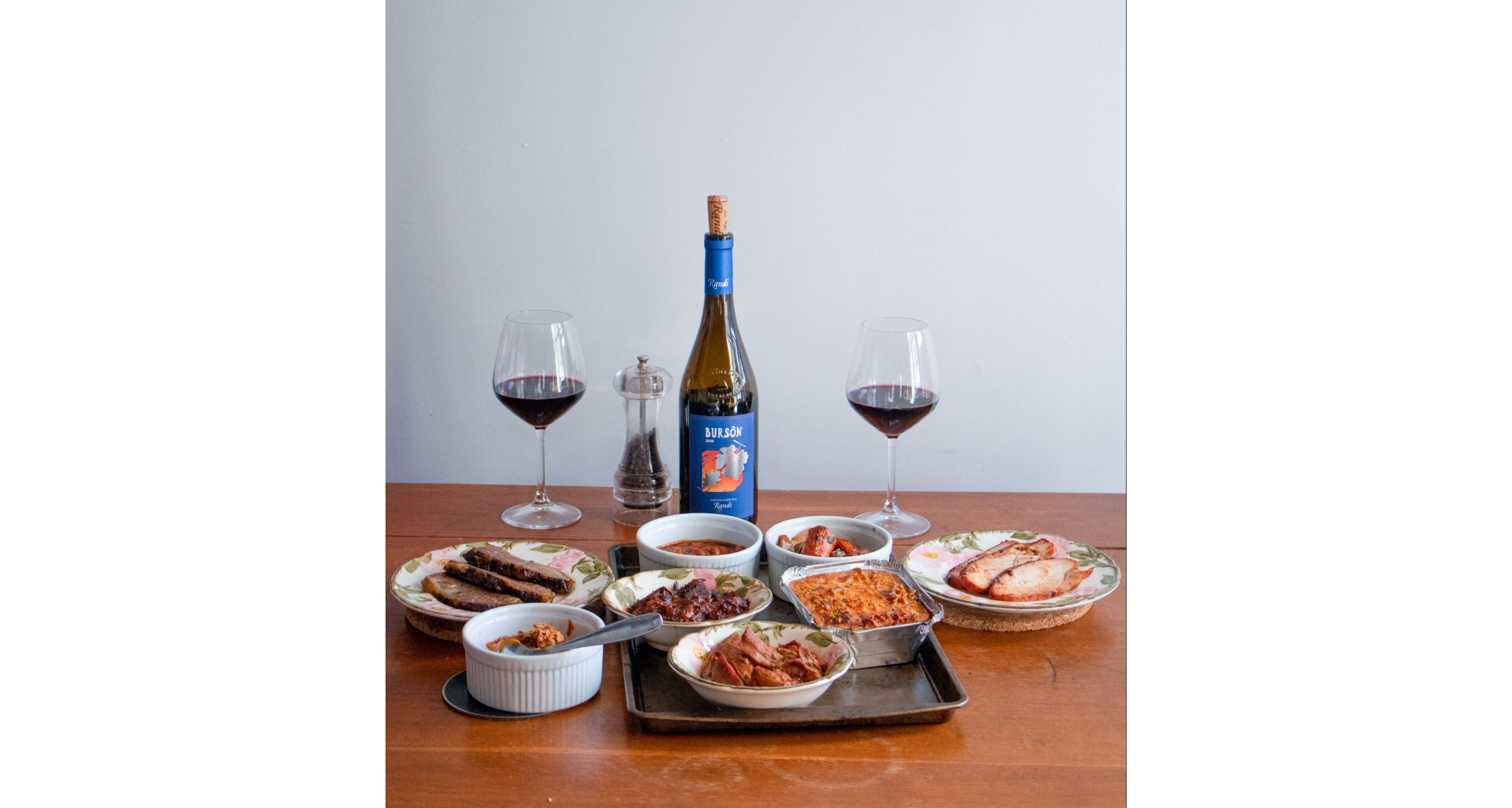 A table with an open bottle, two filled wine glasses and other dishes.