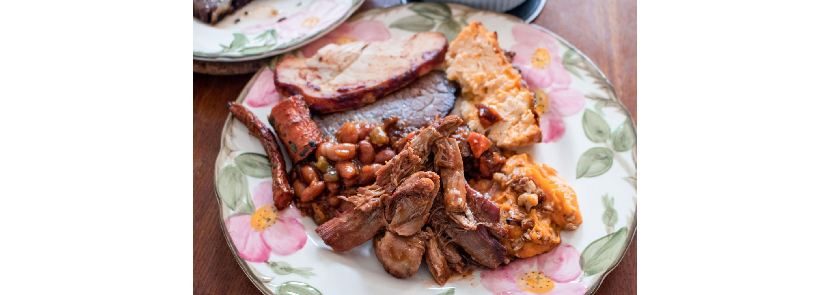 A floral plate filled to the brim with brisket, beans and more.