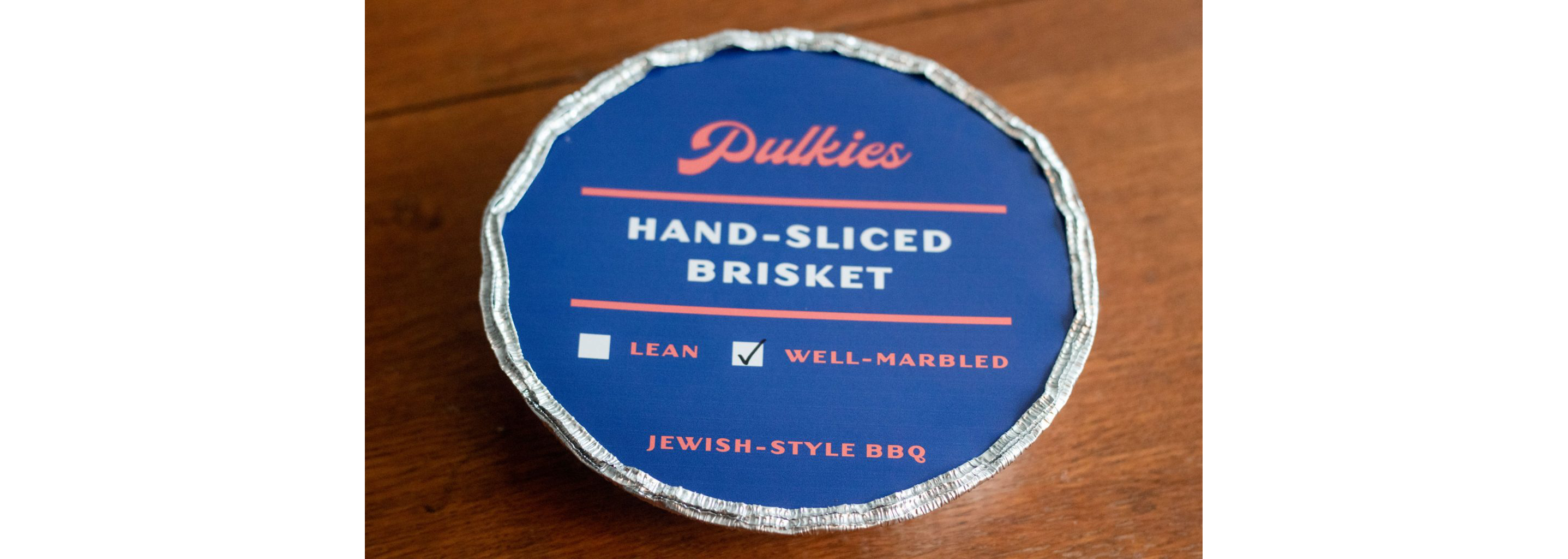 A sealed circular foil container filled with hand-sliced brisket.