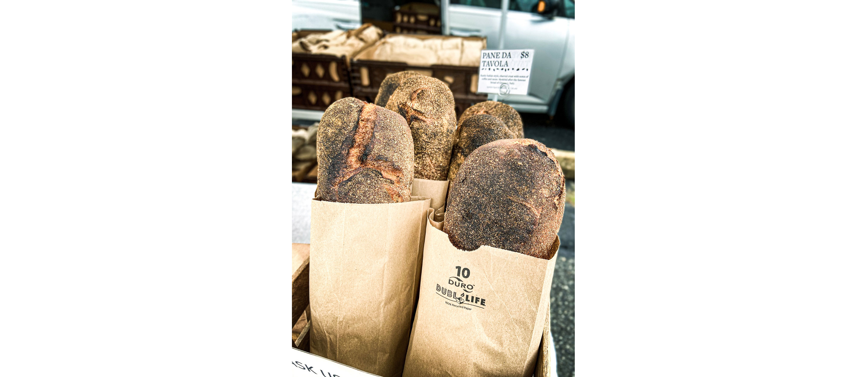 Four loaves of baked bread resting in individual brown paper bags.