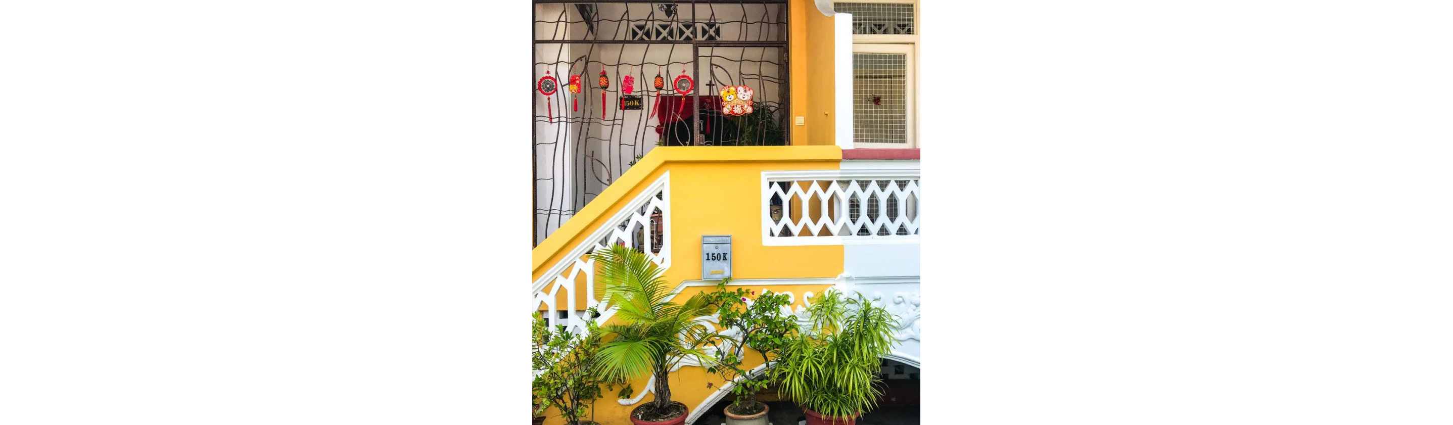 The bright yellow exterior of a home with various plants and Lunar New Year decorations hanging.