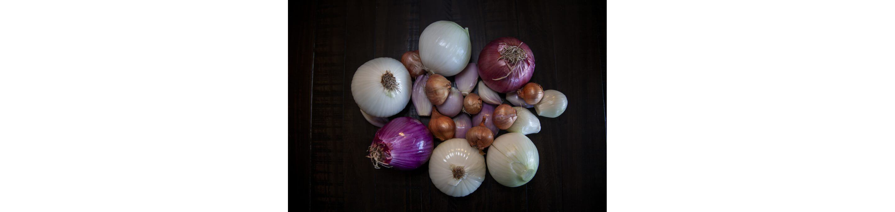 Assorted onions and shallots resting on a dark table.