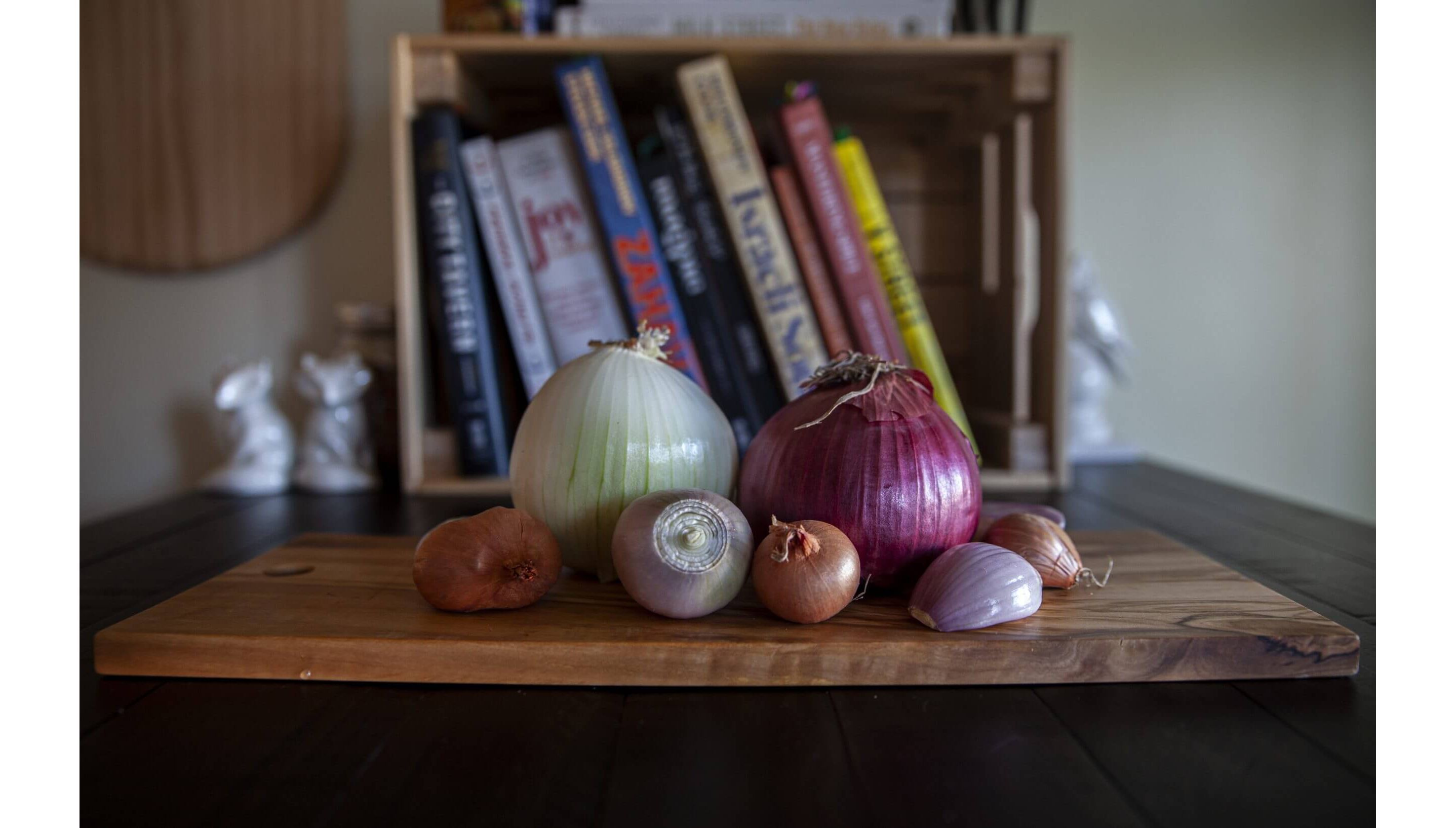 Assorted onions of all shapes and sizes resting on a wooden cutting board.