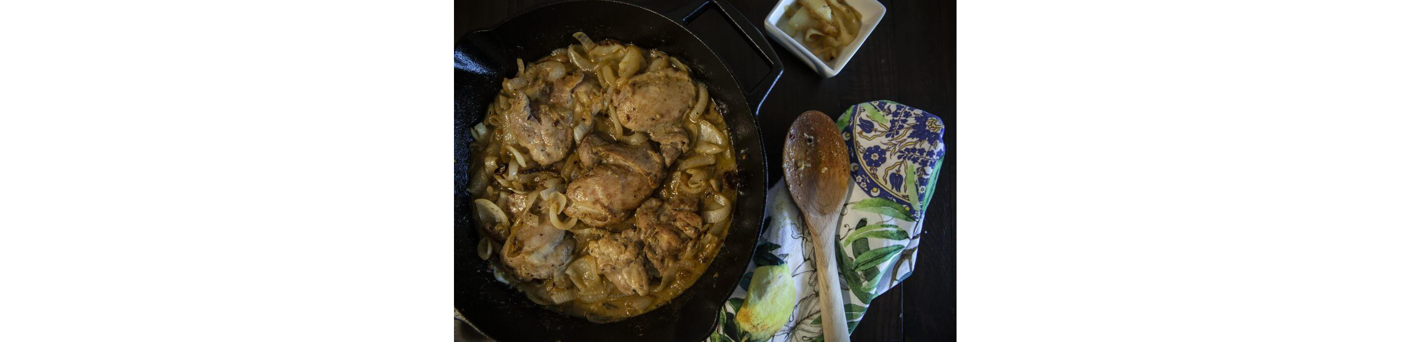 Chicken thighs cooking in a cast iron skillet with caramelized onions.