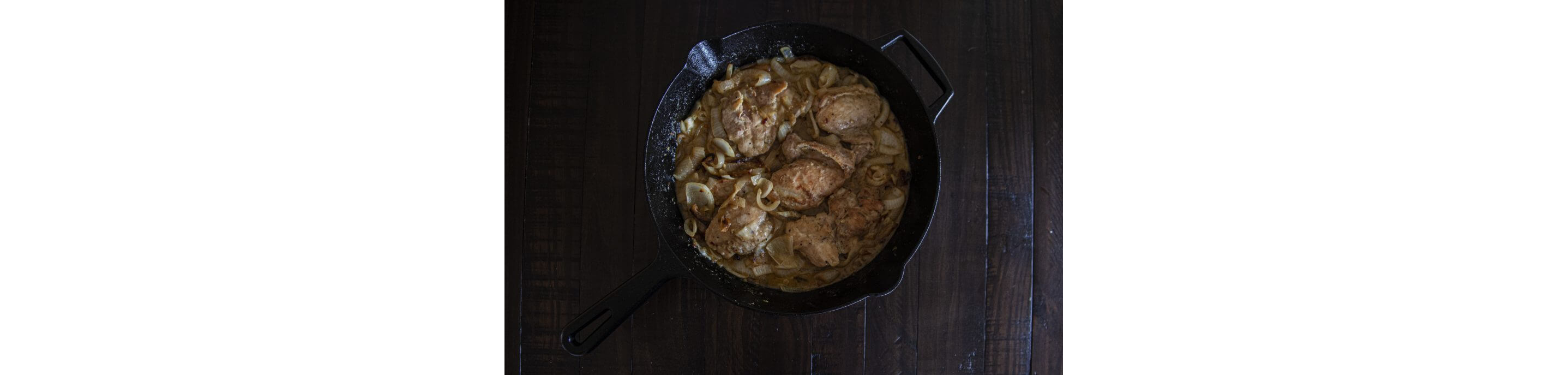 A cast iron skillet holding chicken thighs and caramelized onions.