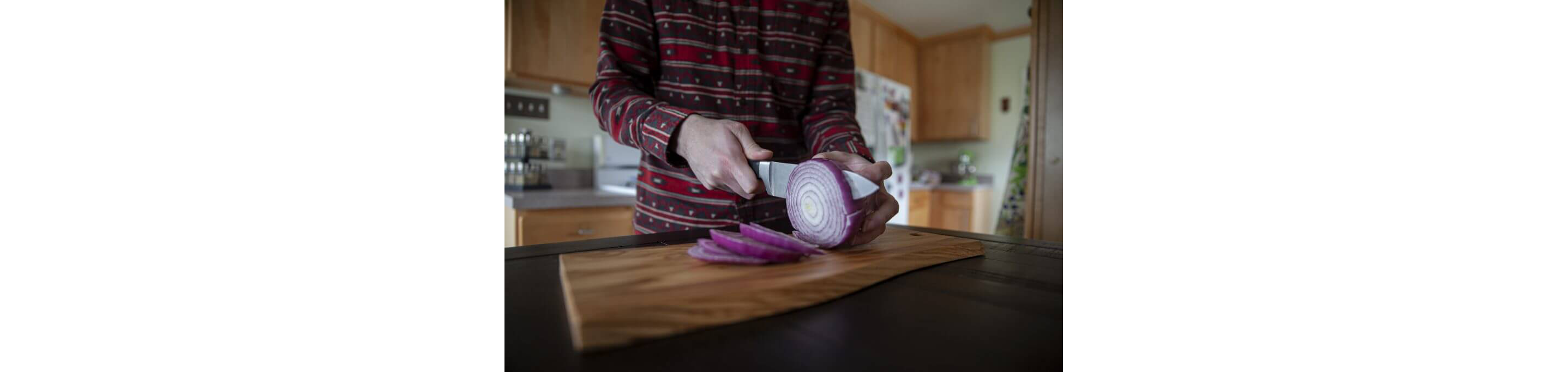 A person slicing a red onion on a wooden cutting board with a large knife.